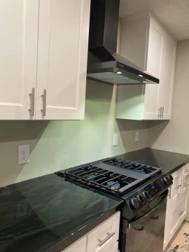 Kitchen with range, white cabinets, and black countertops visible