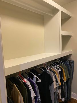 closet with shirts on hangers and an empty wooden shelf flush with the wall